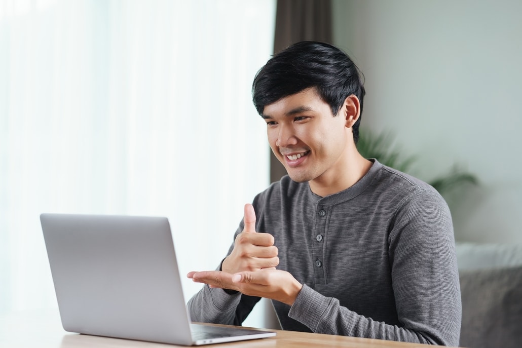 Young Asian man deaf disabled using laptop computer for online video conference call learning and communicating in sign language.